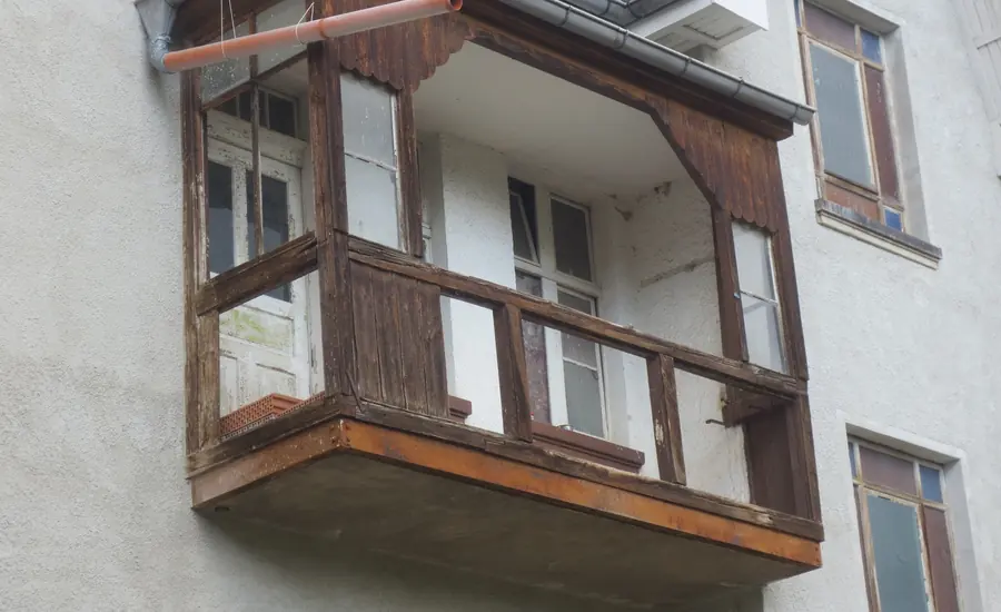 Hölzerner Balkon mit Geländer an der verputzten Fassade eines mehrgeschossigen Wohnhauses