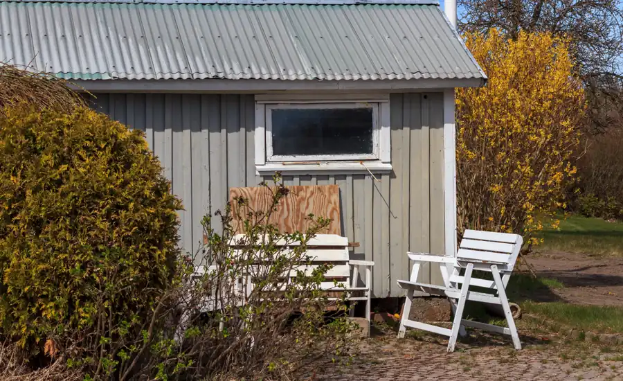 Graues Holzgartenhaus mit weißen Gartenstühlen davor