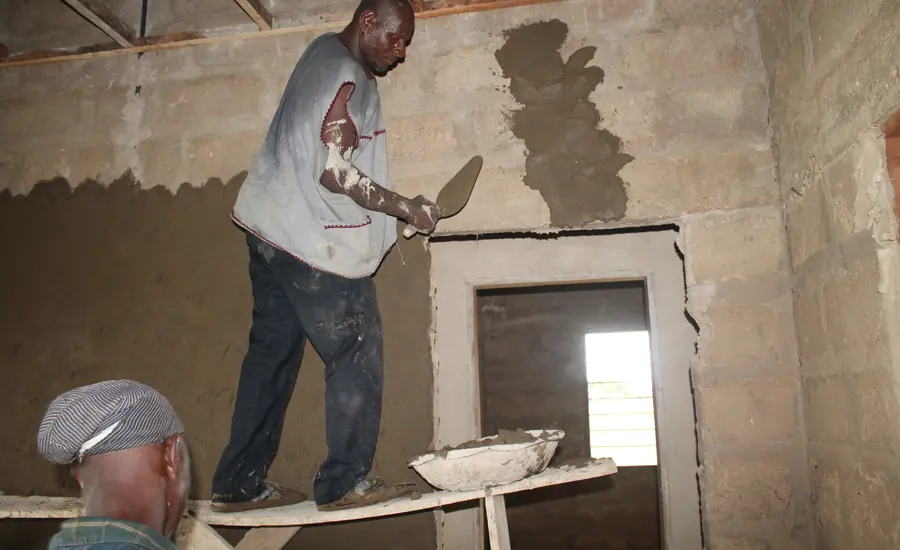 Handwerker trägt mit einer Kelle Putz auf eine Innenwand aus Mauerwerk auf