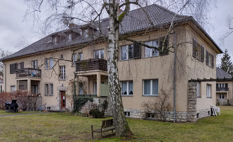 Zweigeschossiges Mehrfamilienhaus mit Walmdach, Balkonen und Fensterläden auf einem großen Rasengrundstück mit Birke und Holzbank in Berlin-Schlachtensee