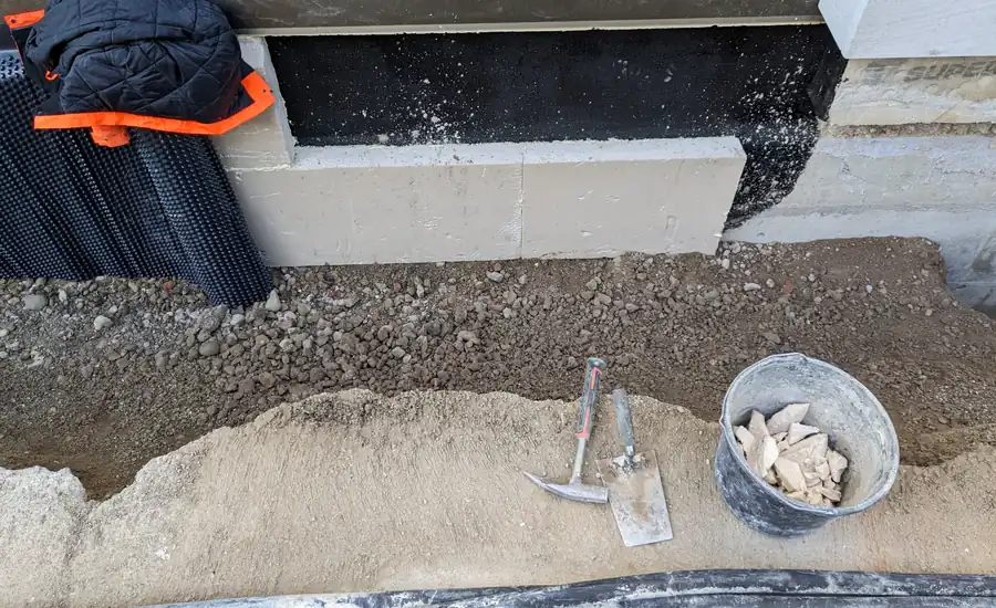 Schwarz abgedichteter Betonsockel einer Kellerwand mit angelegter Noppenbahn im Erdreich