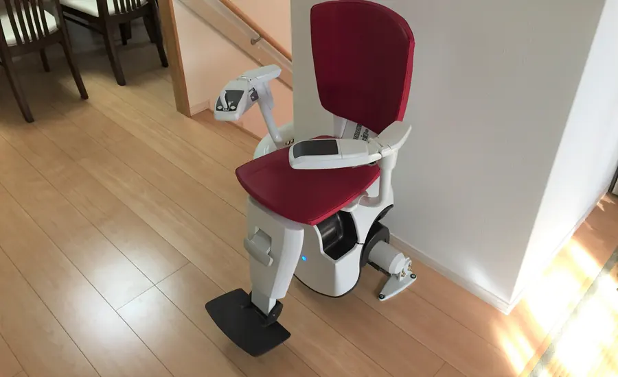 Treppenlift mit rotem Sitz am unteren Ende einer Innentreppe in einem Wohnhaus