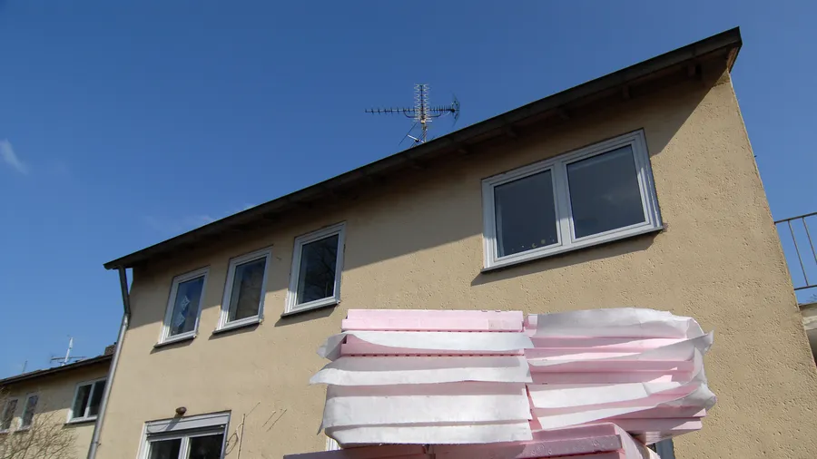 Gestapelte rosafarbene Dämmplatten vor der verputzten Fassade eines Wohnhauses mit Kunststofffenstern
