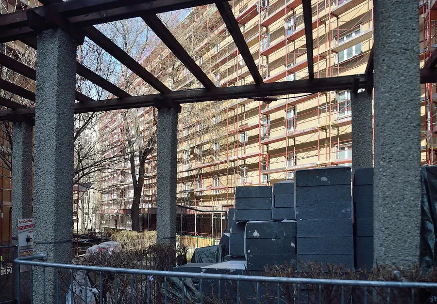 Mehrgeschossiges Wohngebäude mit Gerüst an der Fassade, im Vordergrund gestapelte dunkle Dämmplatten