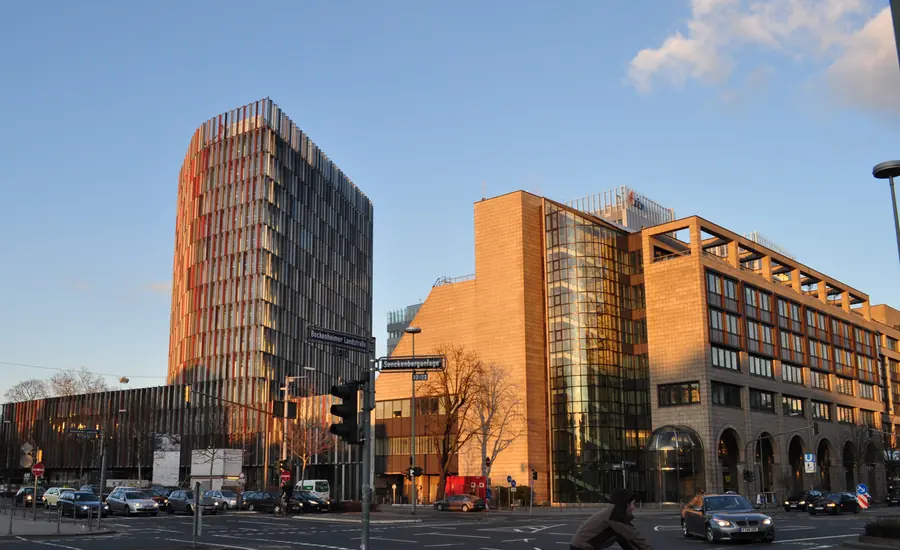 Bürohochhaus mit farbiger Lamellenfassade neben einem niedrigeren Bürogebäude an einer Kreuzung
