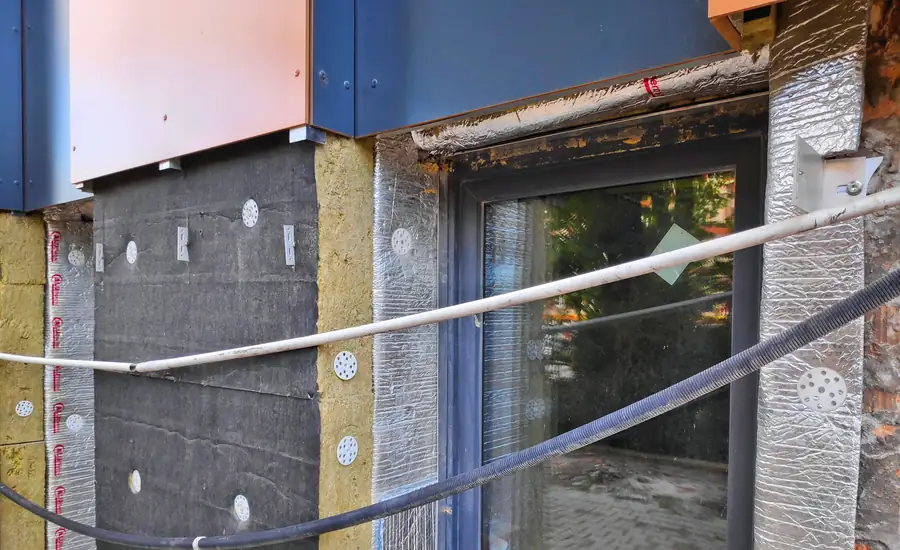 Fassade während einer nachträglichen Wärmedämmung: gedübelte Dämmplatten, Mineralwolle und Aluminiumkaschierung rund um ein großes Fenster