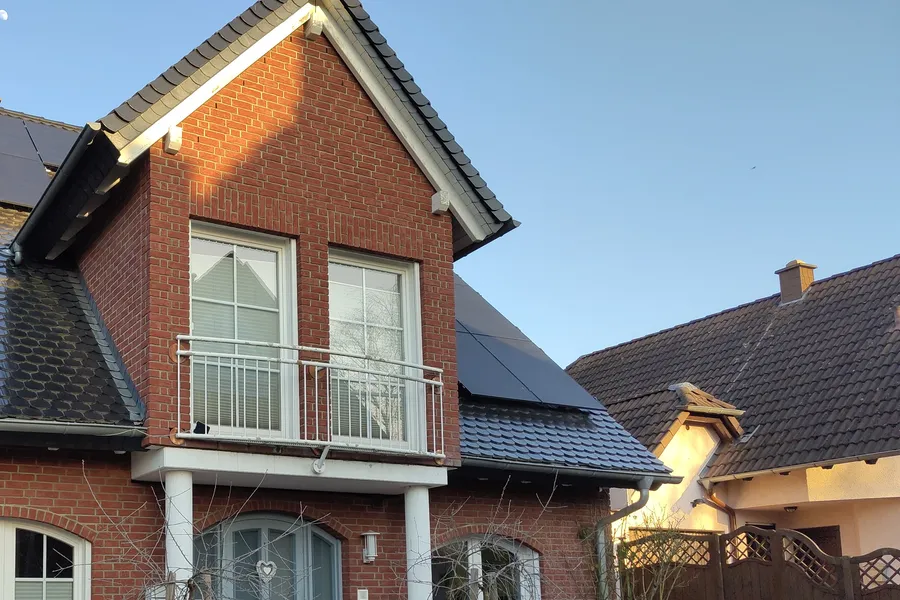 Rotes Backsteinhaus mit Giebelbalkon, auf dem Dach dunkle Photovoltaikmodule neben dunklen Dachziegeln