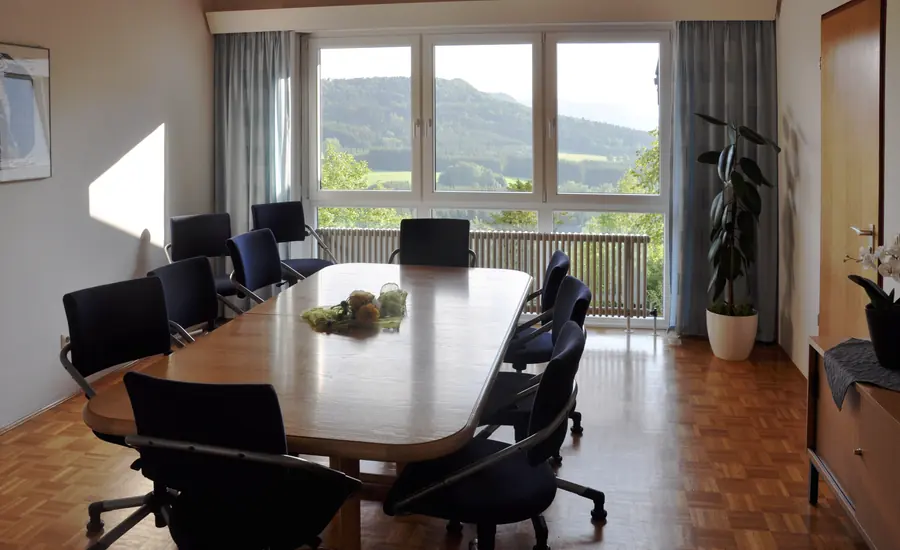 Leerer Besprechungsraum mit langem Tisch, Polsterstühlen und Fensterfront mit Blick ins Grüne
