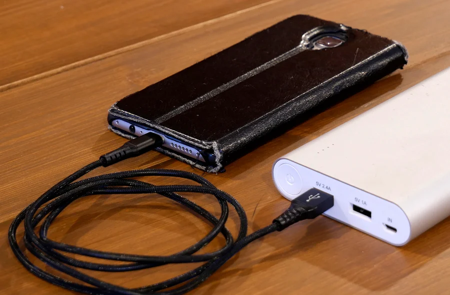 Smartphone mit schwarzer Hülle und USB-Kabel neben dem Anschluss einer weißen Powerbank