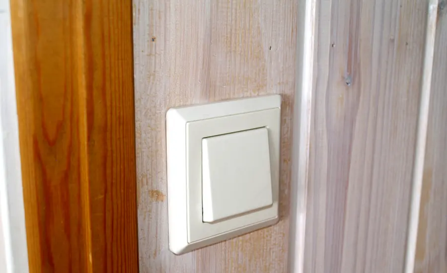 Weißer Lichtschalter an einer Holzwand neben einem Türrahmen