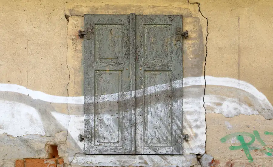 Verwitterte hölzerne Fensterläden in einer alten Putzfassade mit einem durchgehenden Riss im Putz