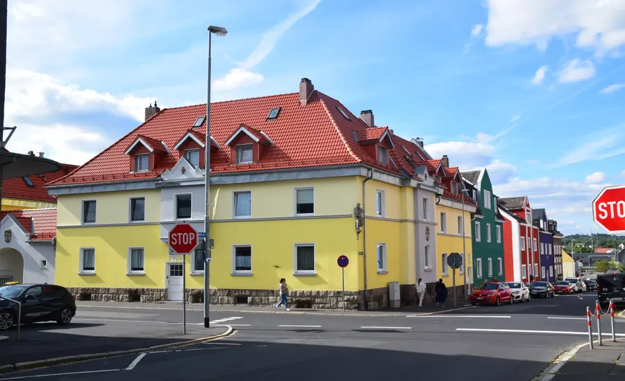 Gelb verputztes Mehrfamilienhaus mit rotem Ziegeldach an einer Straßenkreuzung