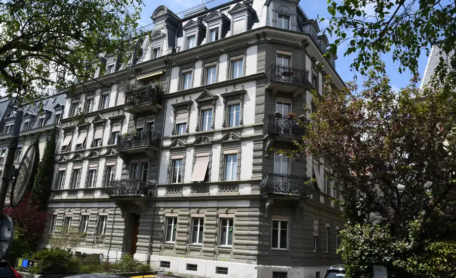 Mehrfamilienhaus mit gegliederter Altbaufassade und Bäumen an der Straße