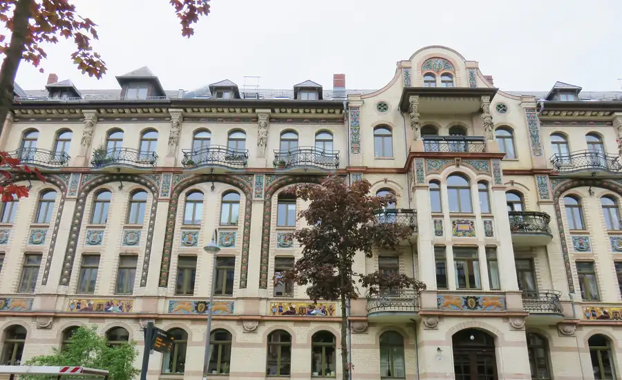 Verzierte Altbaufassade eines mehrgeschossigen Mietshauses, an die links und rechts weitere gleichartige Wohnhäuser anschließen