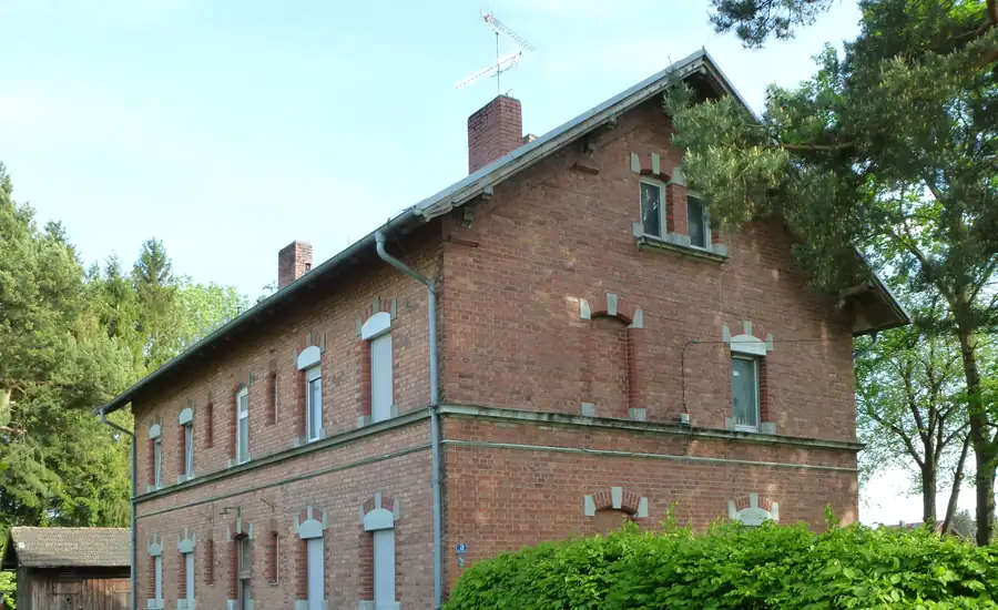 Zweigeschossiges Wohnhaus aus rotem Backstein mit hellen Fenstergewaenden zwischen Baeumen