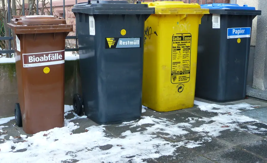 Vier Mülltonnen für Bioabfälle, Restmüll, Gelbe Tonne und Papier nebeneinander auf schneebedecktem Boden