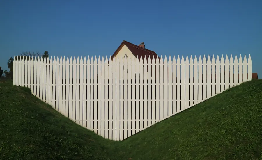 Weißer Lattenzaun entlang einer Grundstücksgrenze vor blauem Himmel
