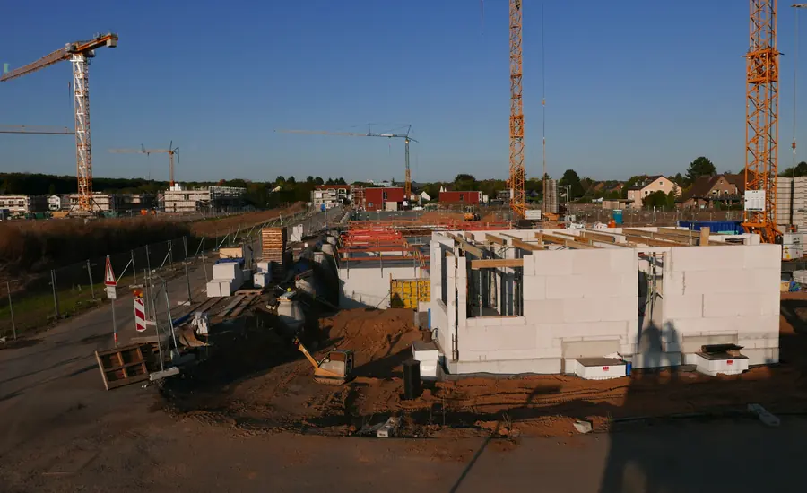 Baustelle in einem Neubaugebiet mit mehreren Rohbauten, Baukränen und Baumaterial