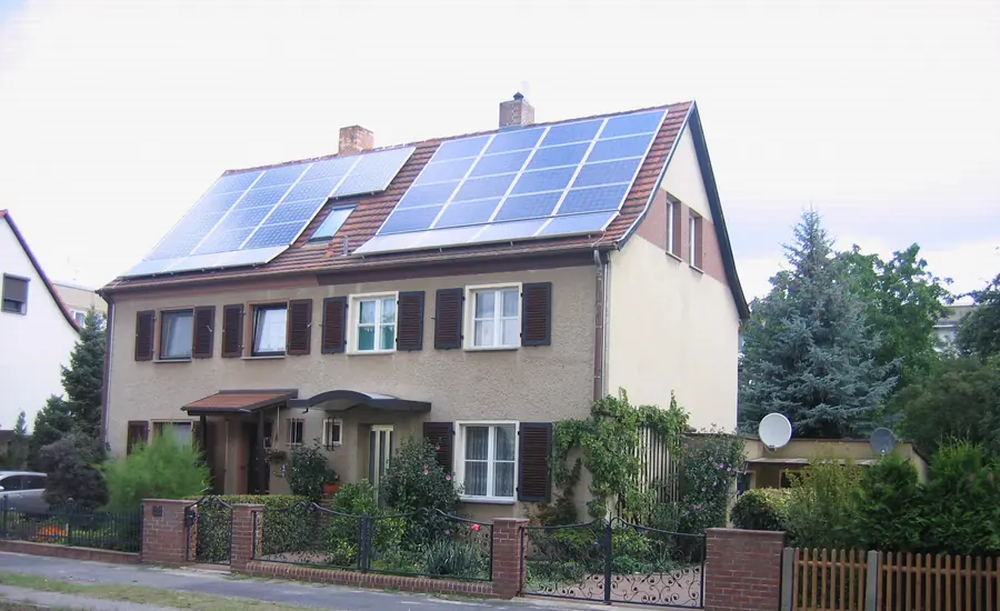 Verputztes Wohnhaus in Cottbus mit zwei Hauseingängen, Photovoltaikanlage auf dem Ziegeldach, dunkelbraunen Fensterläden und eingezäuntem Vorgarten