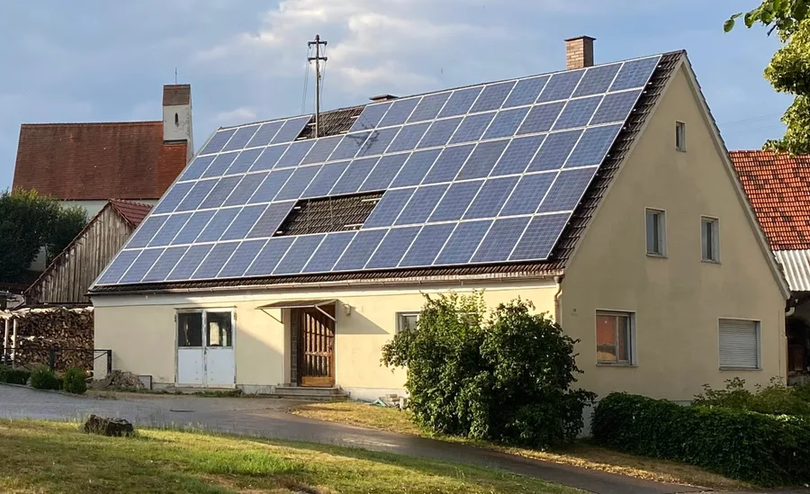 Wohnhaus mit Satteldach, dessen eine Dachfläche fast vollständig mit blauen Photovoltaikmodulen belegt ist