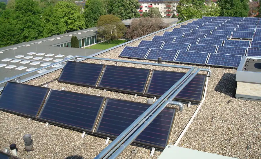 Flachdach mit dunklen Solarthermie-Flachkollektoren und blauen Photovoltaikmodulen nebeneinander
