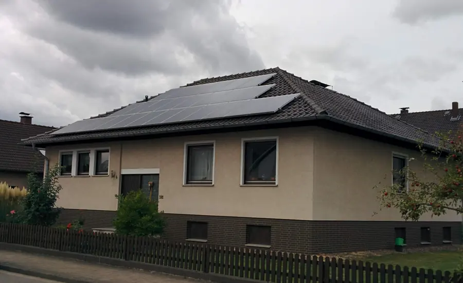 Einfamilienhaus mit Photovoltaikmodulen auf dem Walmdach in Kirchohsen bei Emmerthal, davor ein Holzzaun