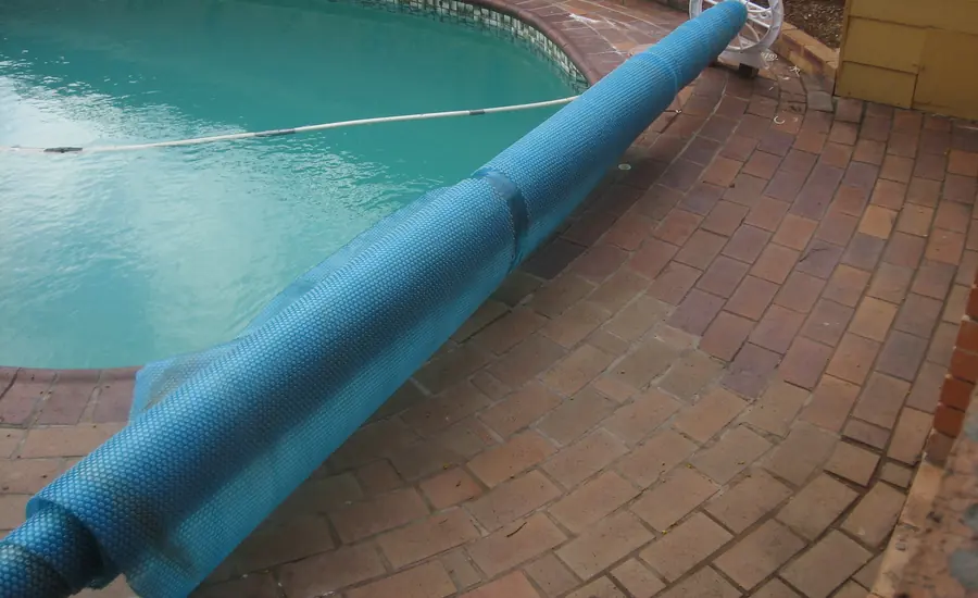 Blaue Poolabdeckung auf einer Aufrollvorrichtung am Beckenrand