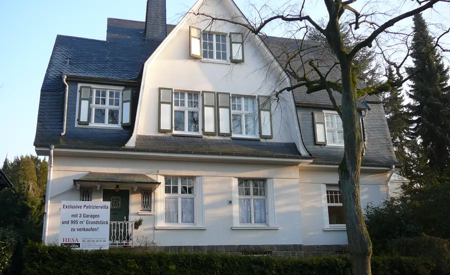 Weiß verputzte Villa mit Schieferdach an der Kaiser-Wilhelm-Allee in Wuppertal, am Eingang hängt ein Maklerschild „zu verkaufen!“