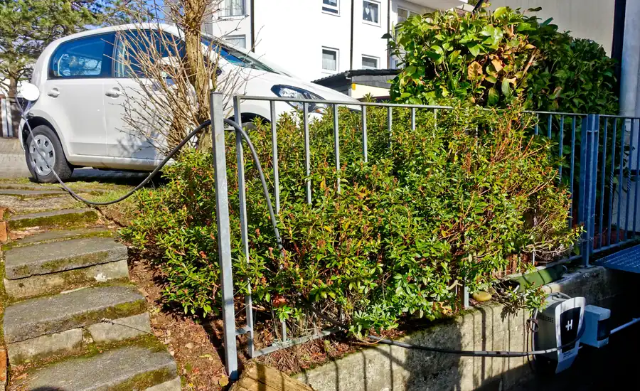 Ladekabel einer privaten Wallbox führt über einen Vorgartenzaun zu einem weißen Auto