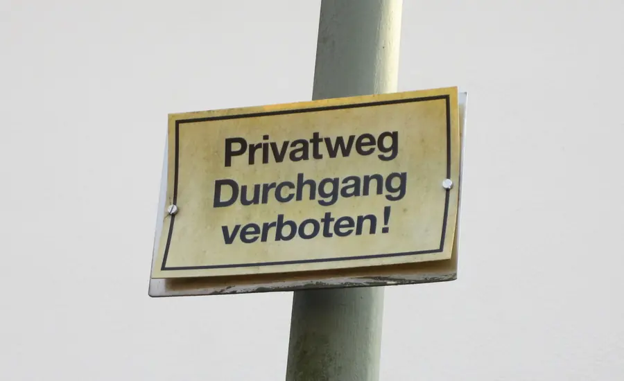 Vergilbtes Blechschild mit der Aufschrift „Privatweg – Durchgang verboten!“ an einem Metallpfosten in Moosburg an der Isar