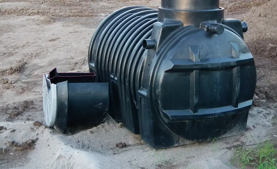 Schwarzer Kunststofftank einer Regenwasserzisterne mit Filterschacht in einer Sandgrube