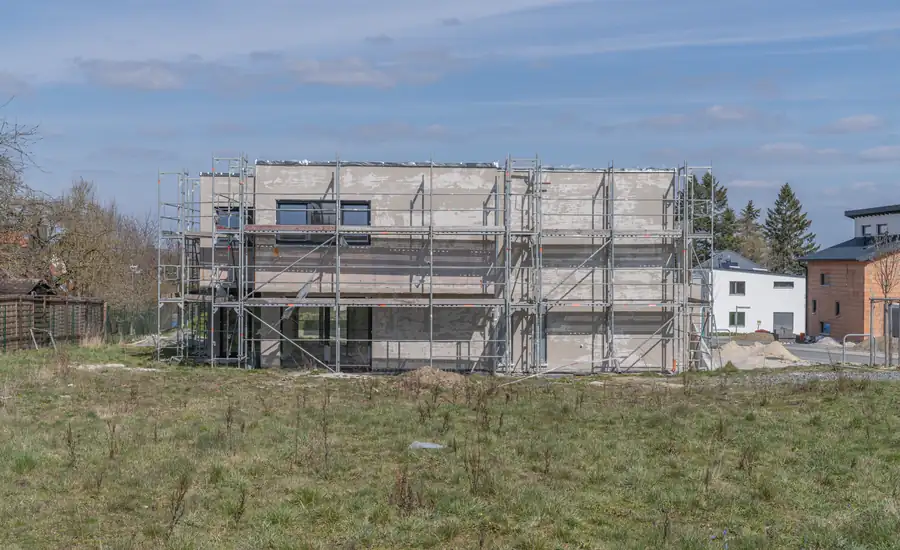 Eingerüsteter Rohbau eines Wohnhauses auf einer unbebauten Wiese im Neubaugebiet