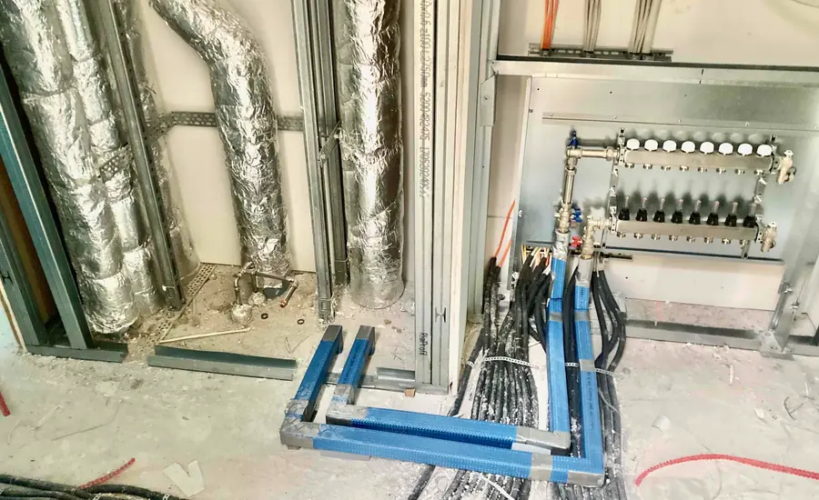 Blau gedämmte Rohrleitungen am Boden, mit Folie ummantelte Steigleitungen und ein Heizkreisverteiler im Rohbau eines Wohnblocks in Bonn