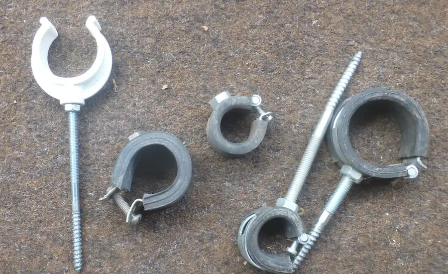 Mehrere Rohrschellen mit Gummieinlage und Stockschrauben auf einer Steinfläche