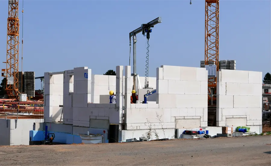 Rohbau eines Einfamilienhauses aus Kalksandsteinwänden mit Versetzgerät und zwei Bauarbeitern, dahinter Baukräne im Neubaugebiet Efferen West bei Hürth