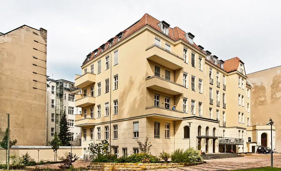Sanierter Altbau mit hellgelber Putzfassade, Balkonen und Vorgarten