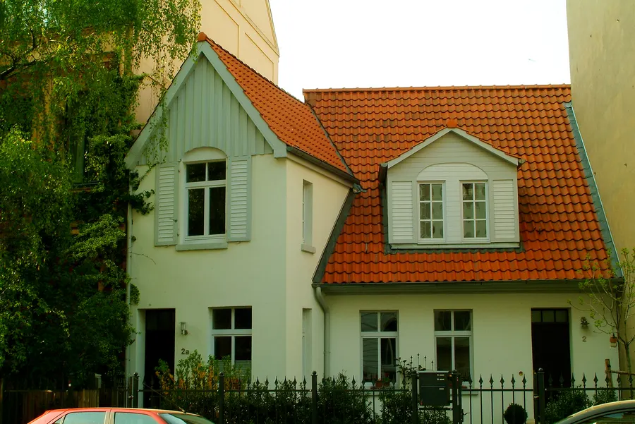 Zwei schmale Einfamilienhäuser mit rotem Ziegeldach, Dachgaube und Vorgartenzaun
