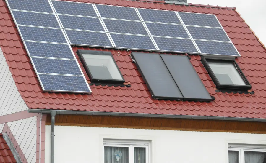 Photovoltaikmodule und dunkle Kollektoren auf einem roten Ziegeldach mit Dachfenstern