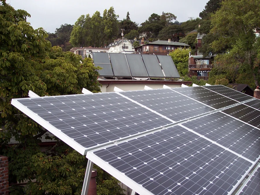 Photovoltaikmodule im Vordergrund und Solarthermie-Kollektoren auf dem dahinterliegenden Hausdach