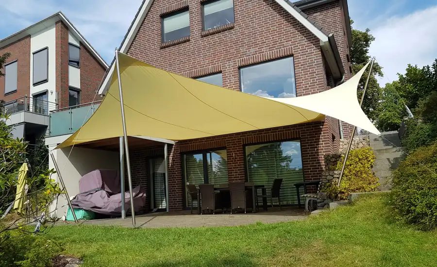 Cremefarbenes Sonnensegel über der Terrasse eines Klinkerhauses mit Gartenmöbeln