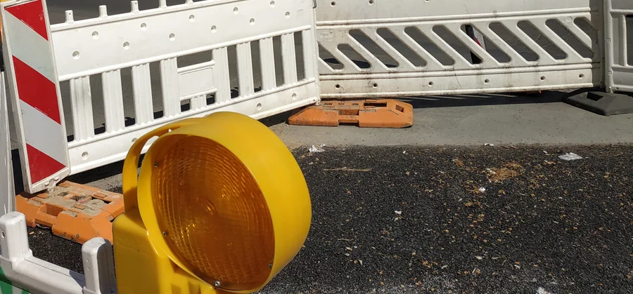 Gelbe Warnleuchte und rot-weiße Absperrung vor einer aufgebrochenen Asphaltfläche