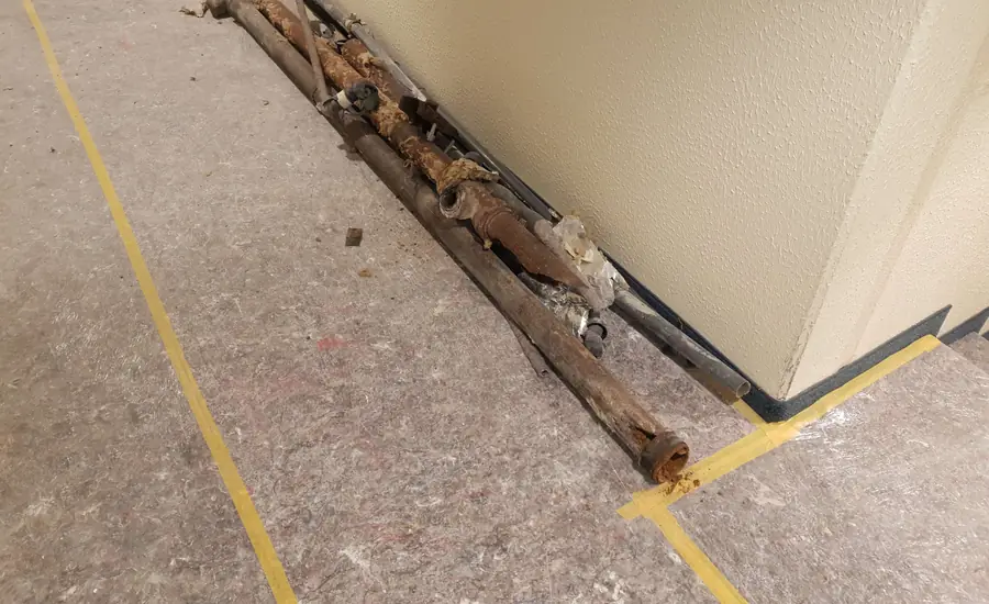 Alte, verrostete Wasserrohre liegen nach dem Ausbau auf abgeklebtem Schutzvlies an einer Flurwand in einem Wohngebäude