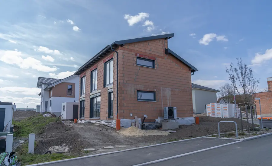 Einfamilienhaus im Rohbau aus Ziegelmauerwerk mit Pultdach im Neubaugebiet Rosenbühl in Hof, daneben bereits fertige Häuser
