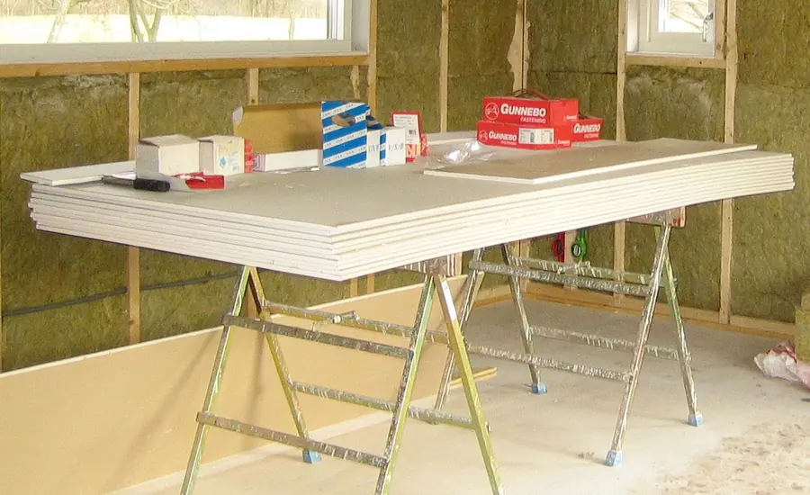 Stapel Gipskartonplatten auf Böcken vor einer gedämmten Ständerwand