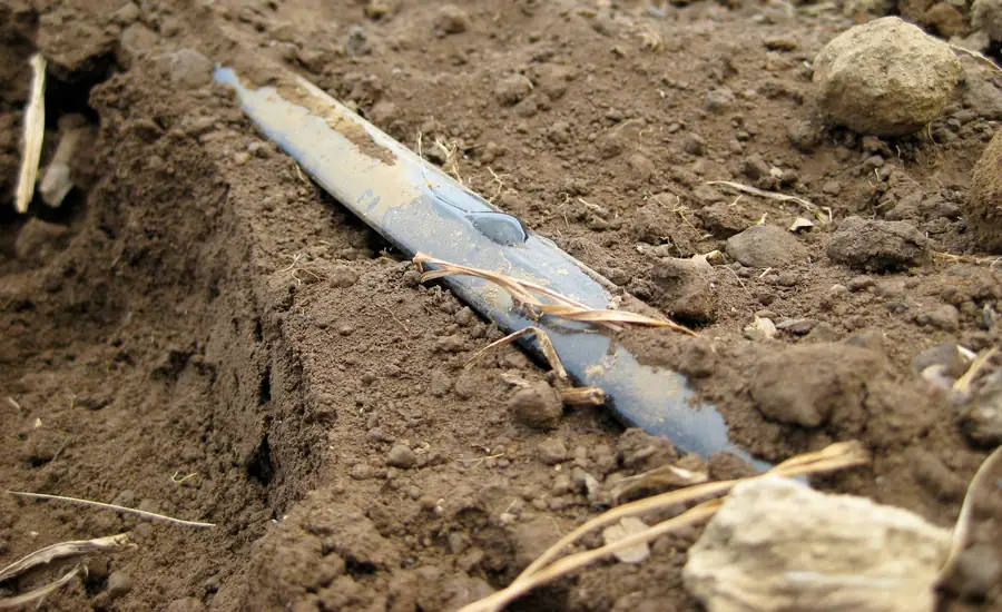 Flacher Tropfschlauch liegt auf brauner Erde zwischen kleinen Steinen