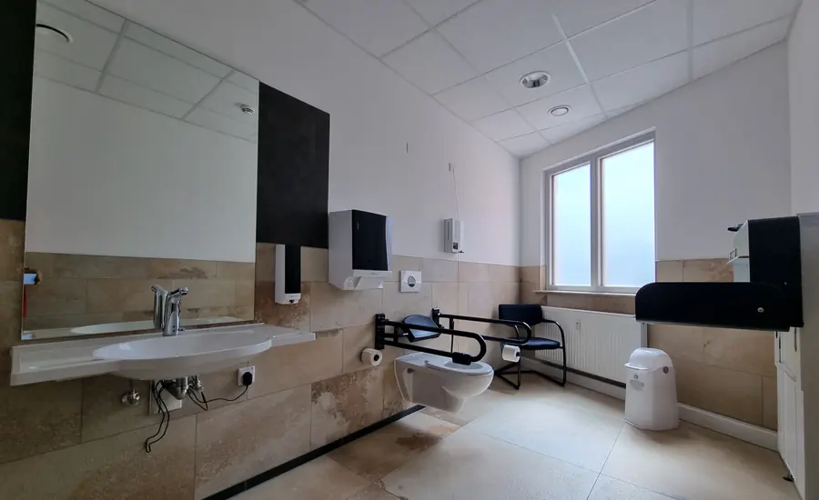 Geräumiges barrierefreies WC in Nürnberg mit unterfahrbarem Waschbecken, klappbaren Stützgriffen am Wand-WC und freier Bewegungsfläche davor