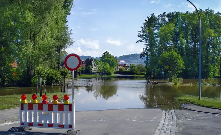 Überflutete Straße mit Absperrschranke und Verkehrsschild am Ortsrand