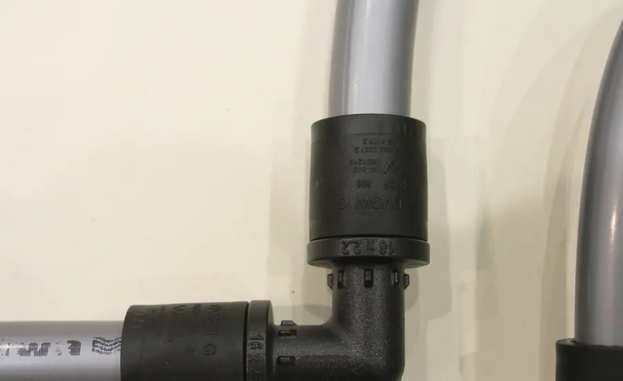 Graue Verbundrohre mit schwarzen Schiebehülsen-Fittings vor einer hellen Wand