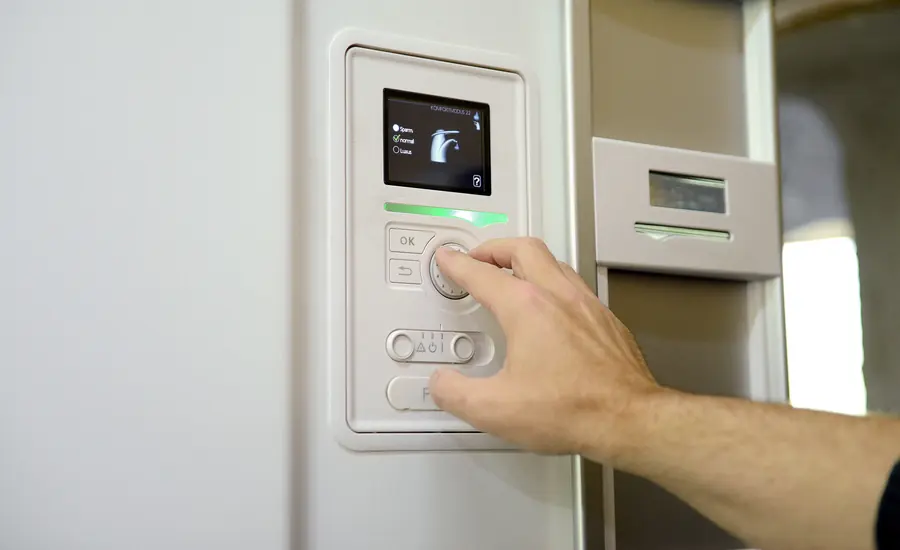 Hand bedient das Display einer Wärmepumpen-Regelung an der Wand