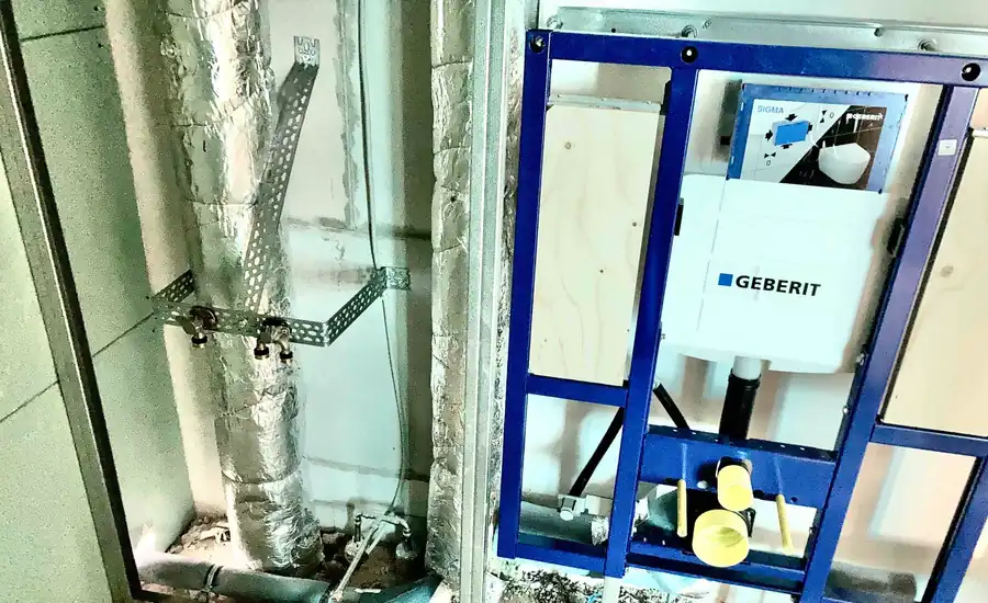 Blaues Vorwand-Installationselement für ein Wand-WC mit Unterputzspülkasten im Rohbau eines Wohnblocks in Bonn, daneben gedämmte Leitungen im Schacht